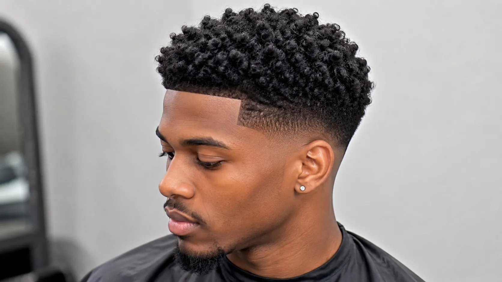 A young man with defined natural curls on top and a sharp mid fade haircut on the sides, showing a clean hairline and modern textured hairstyle.