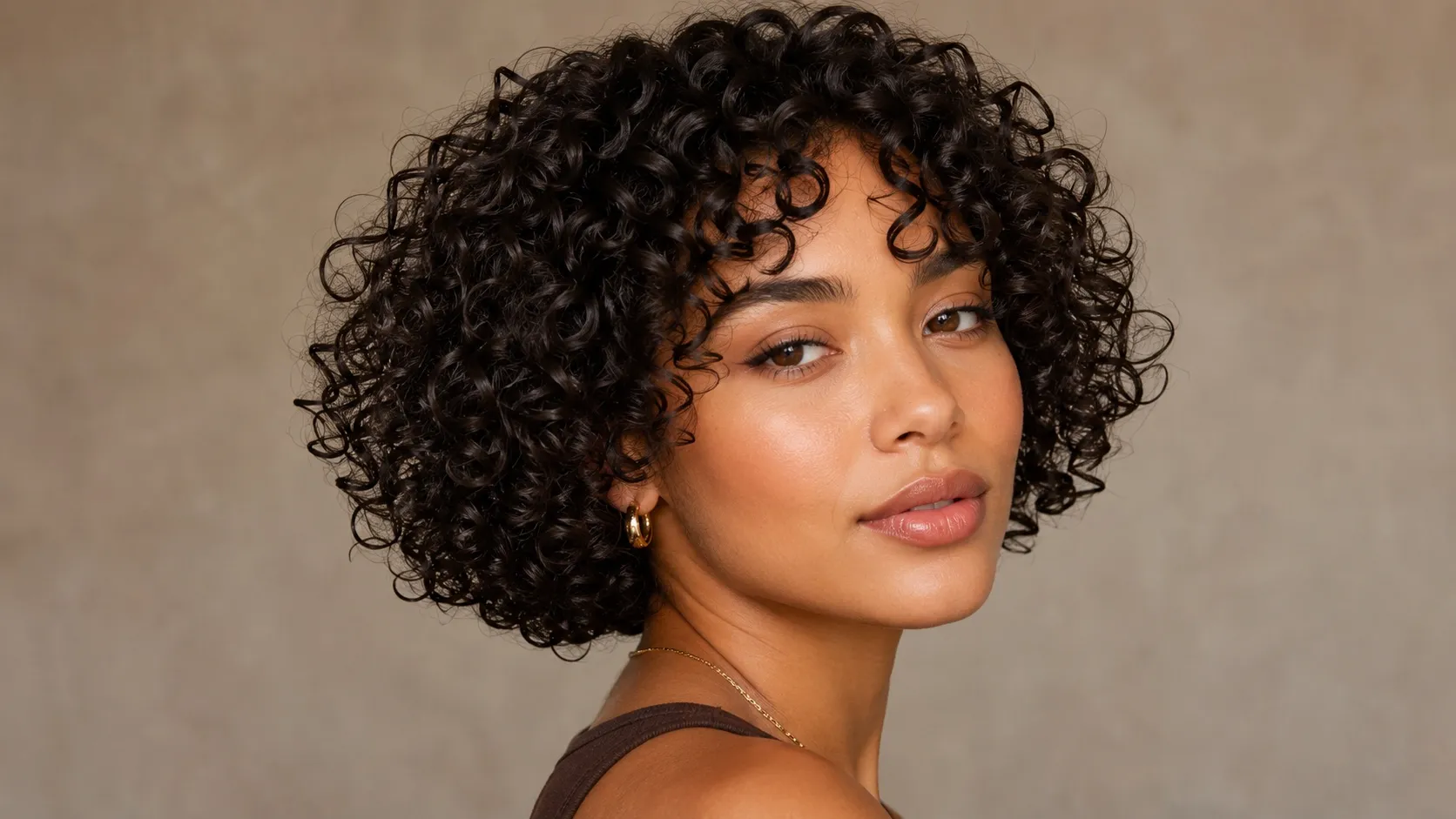 A woman with a short curly bob haircut featuring defined, glossy corkscrew curls that create a rounded silhouette around her face.
