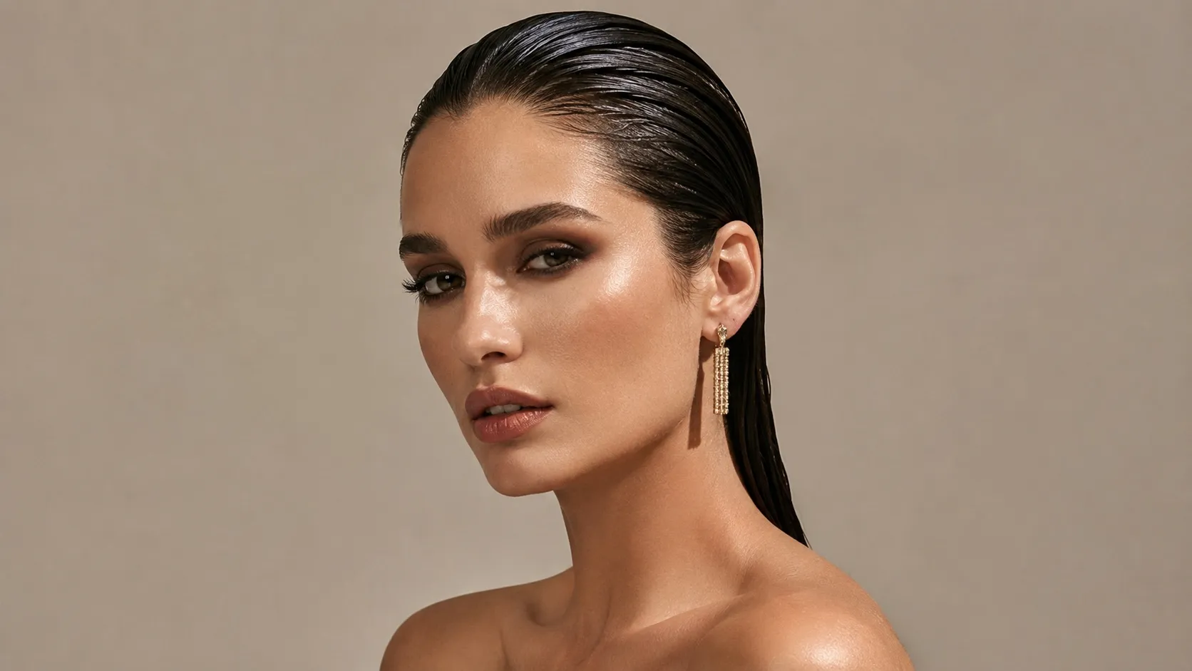 Fashion model with glossy, slicked-back wet-look hair, smoky makeup, and elegant gold earrings against a neutral beige background.