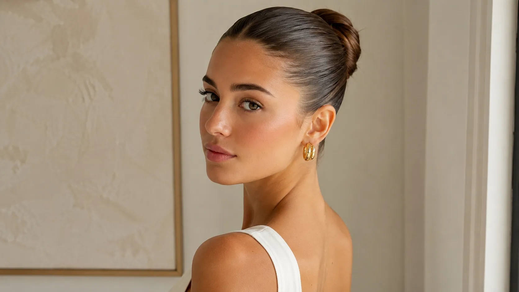 Woman wearing a sleek slicked-back bun with glossy hair, minimal makeup, and a clean, elegant look.