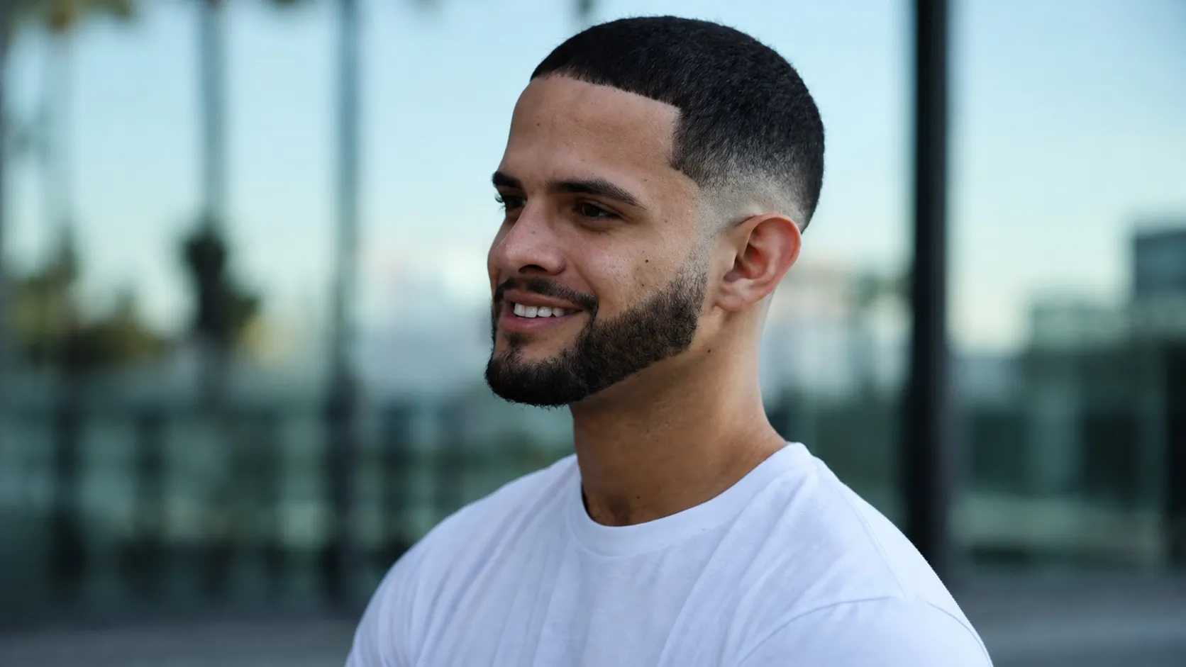 A close-up portrait of a man with a clean low fade buzz cut hairstyle and a neatly lined-up short boxed beard.