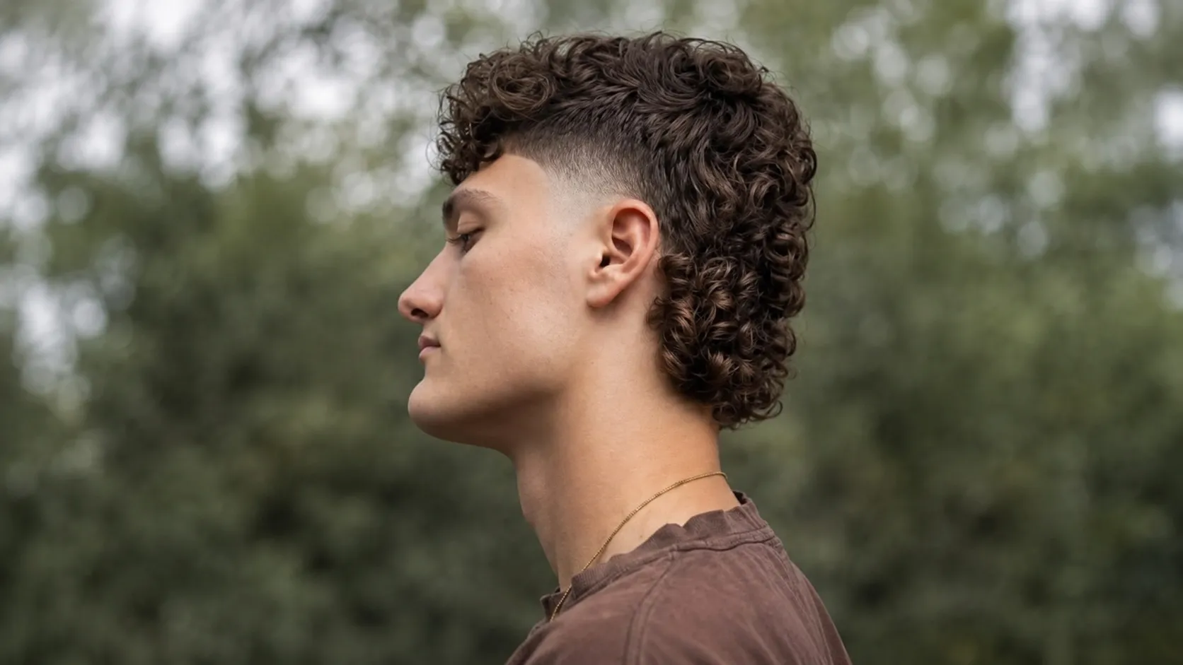 A man with a short curly crop haircut featuring defined, frizz-free curls and tapered sides styled with low-shine pomade