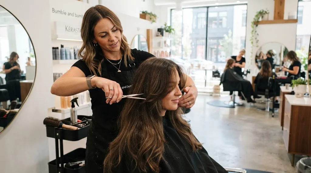 Professional hairstylist demonstrating precision slide-cutting and front layering techniques on long, dense Indian hair in a modern salon.