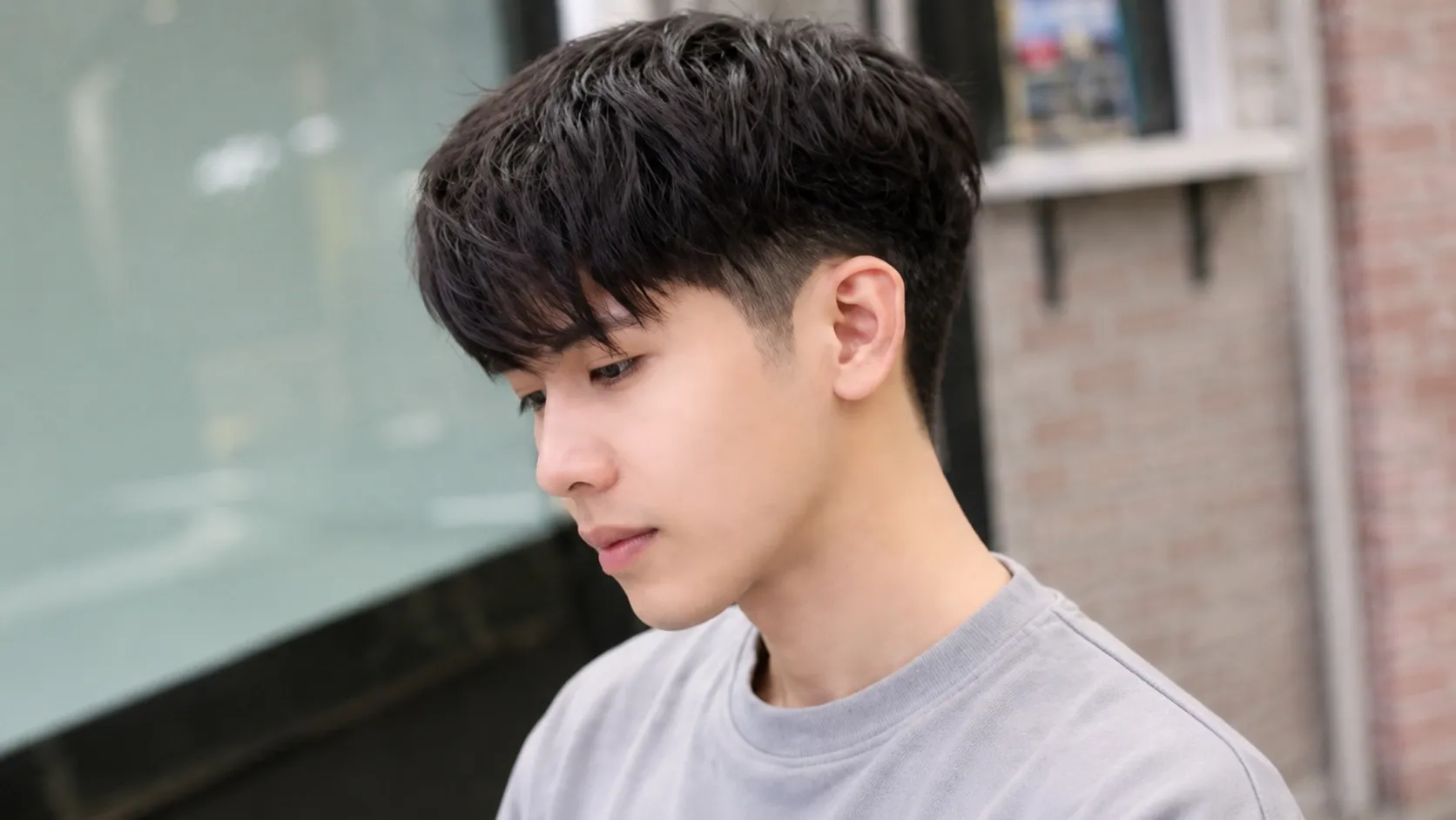 Front and side profile view of a man with a modern Korean two-block haircut featuring short faded sides and a textured layered top.