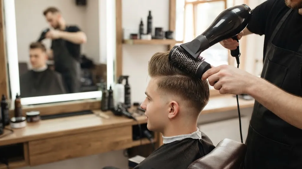 Barber using a blow-dryer and round brush to lift and fix a flat short pompadour hairstyle.